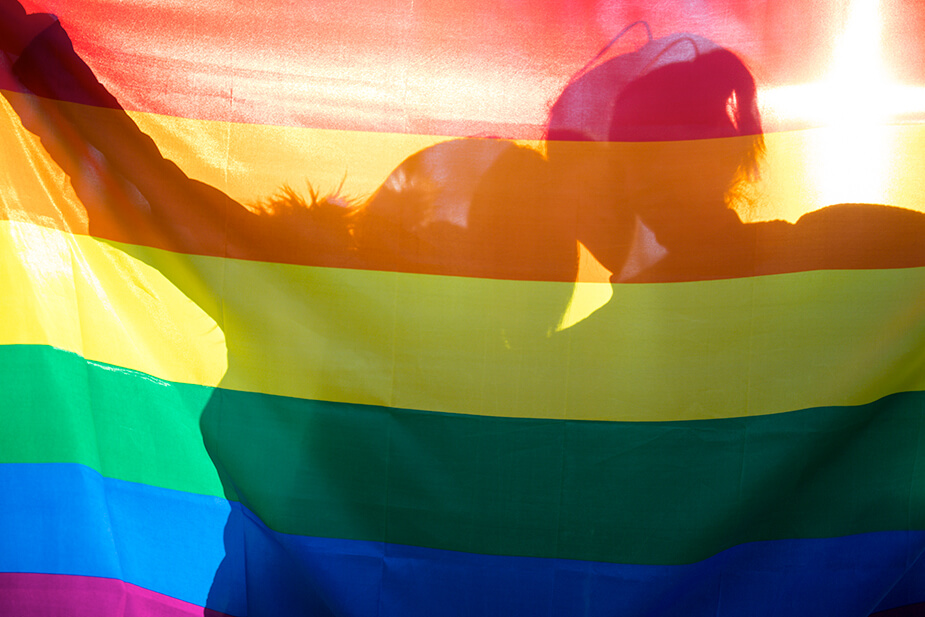 Two women silhouette behind a rainbow flag